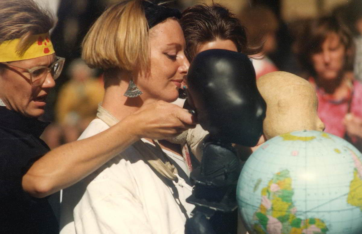 women with abstract puppet figures 1 black and 1 white sharing the carrying of a world globe