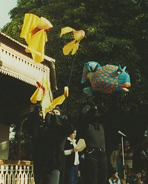 2 people outside parkrotunda holding aloft large brightly-coloured fabric goldfish on sticks