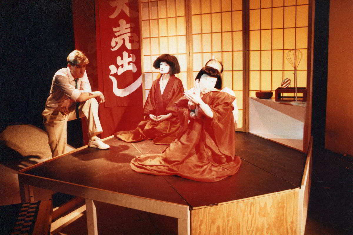 male actor in white leaning towards a woman and her puppet alter ego in red in Japanese tatami-room style setting