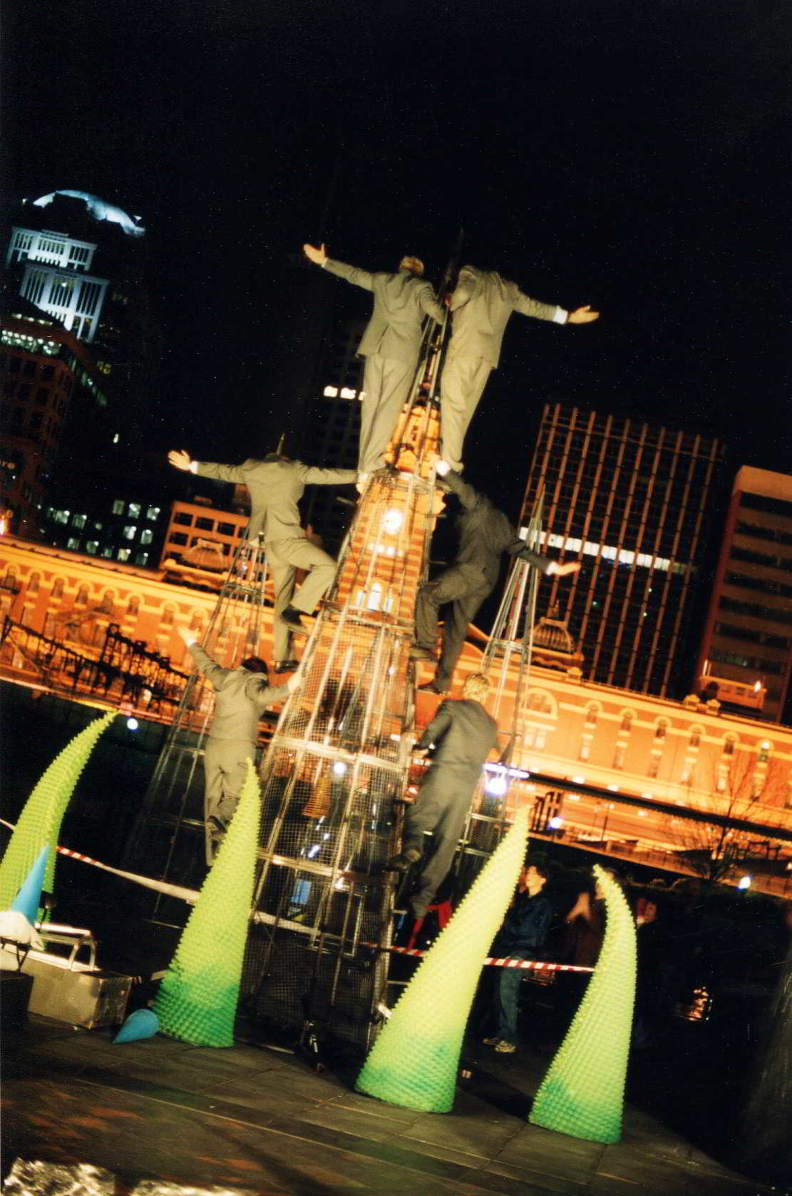 back view of acrobats at night in a 3-high tower in front of city buildings