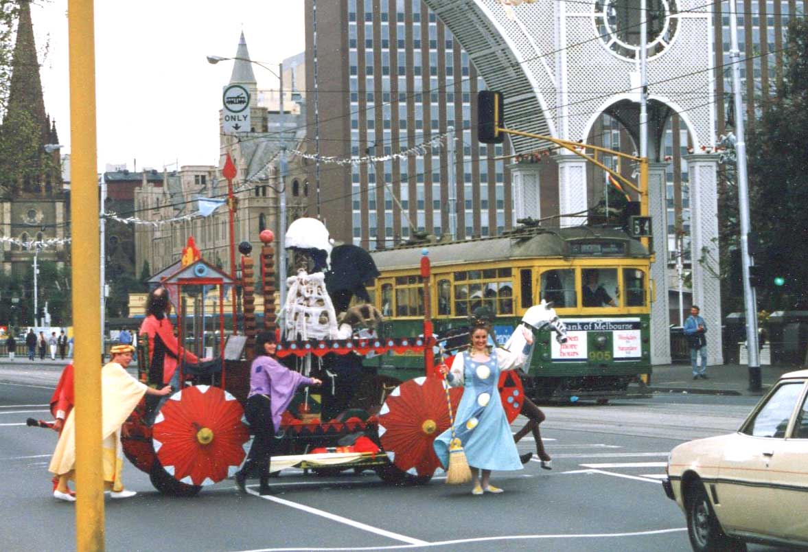 colourful float with red parasol wheels pushed by costumed performers across a city street