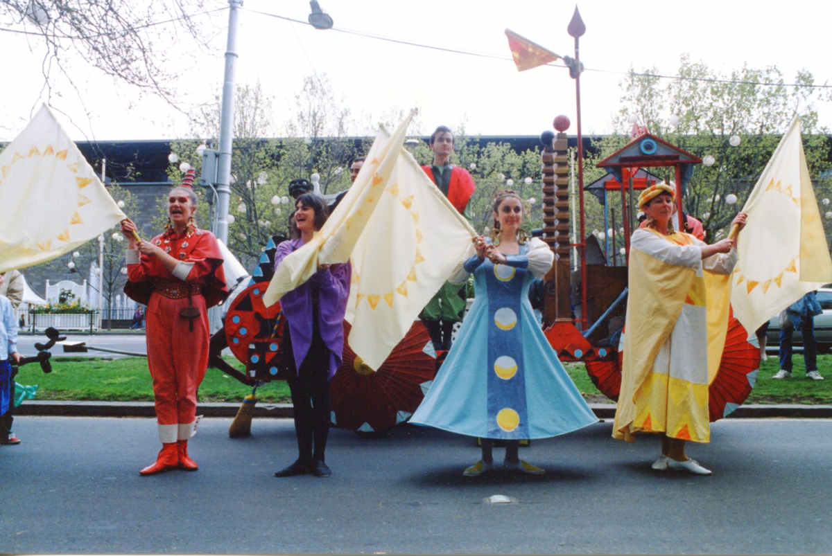costumed performers in front of float waving large colourful flags on city street outside National Gallery of Victoria