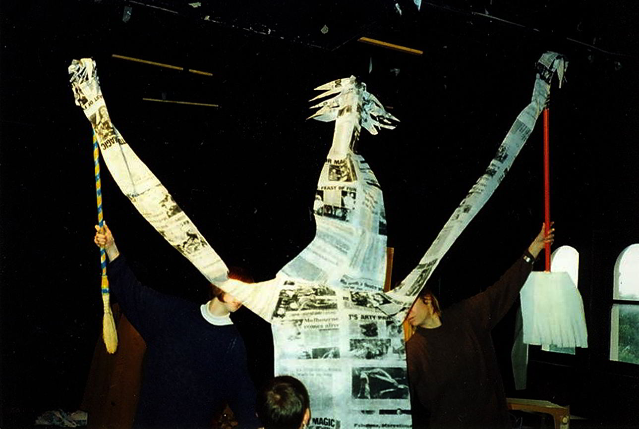 Handspan Theatre Daze of Our Lives Newspaper rod puppet with small head of spiky hair and pointy nose and very long arms pointing upwards