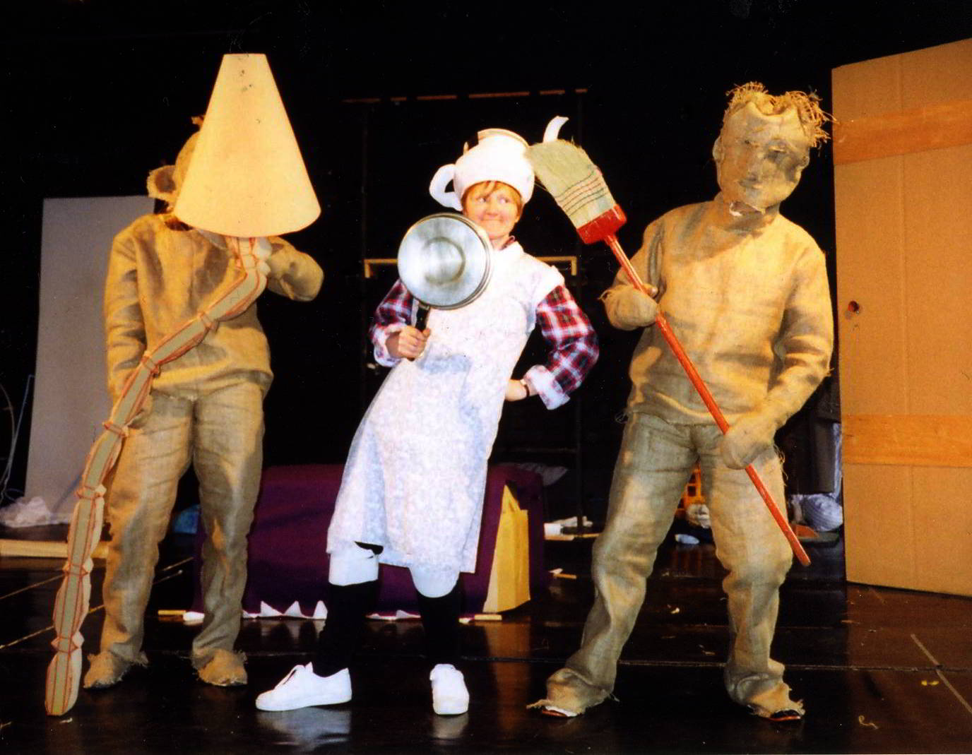 Handspan Theatre Daze of Our Lives hessian bag figures holding a lampshade (L) and a broom (R) in dance rehearsal with woman dressed in white holding a saucepan