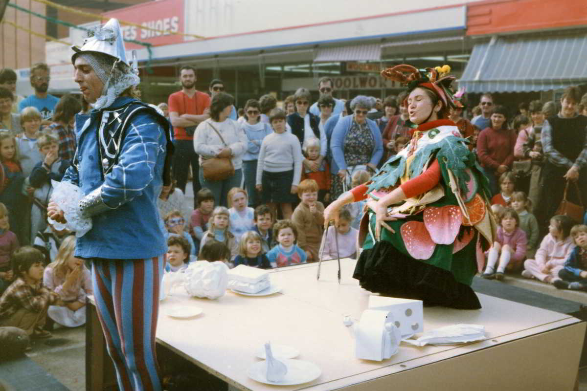 Handspan Theatre Guts table set up in a crowded street with white food objects and performers dressed as king and prince