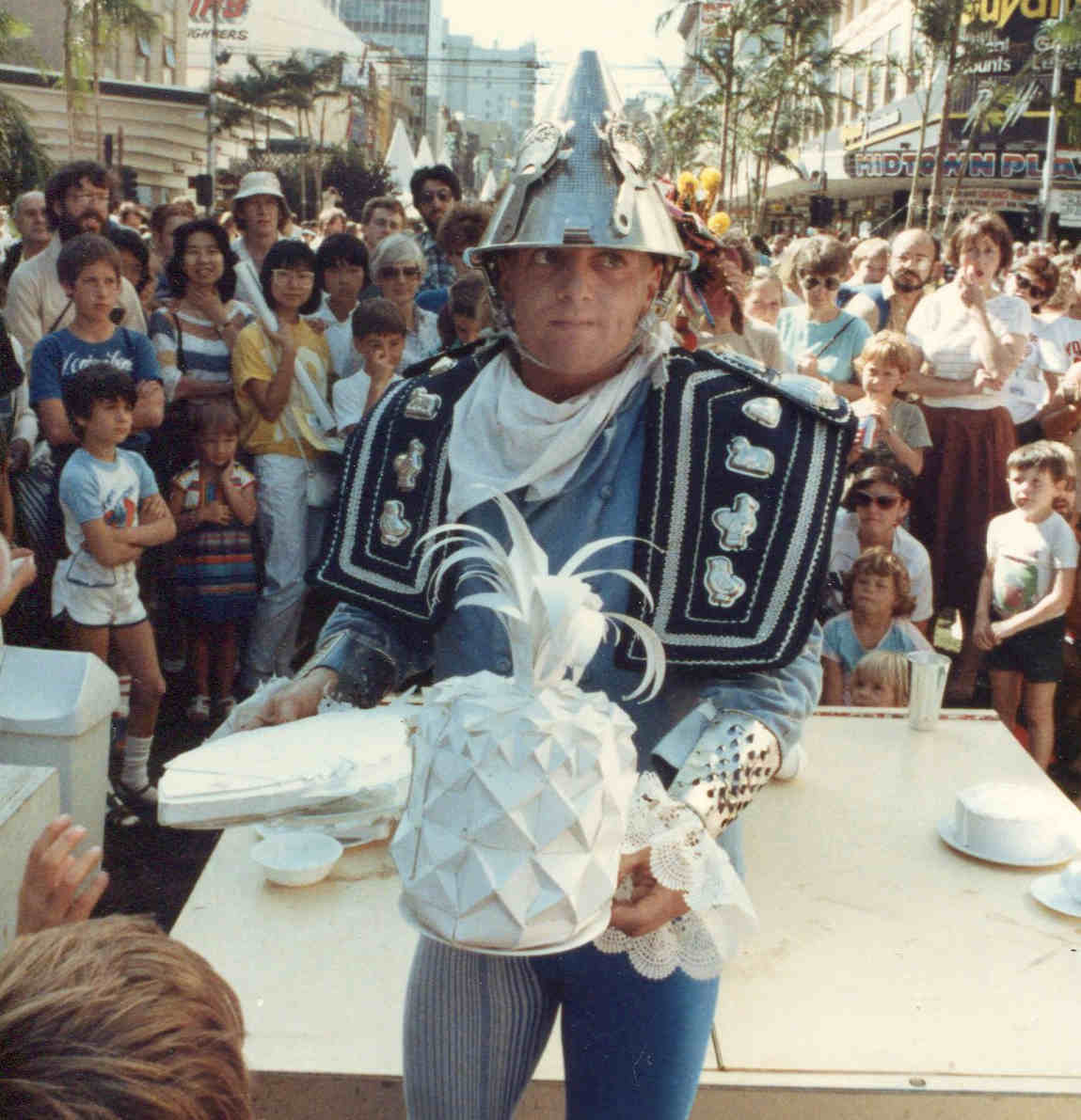Handspan Theatre Guts costumed actor in blue with colander helmet holding white cardboard pineapple