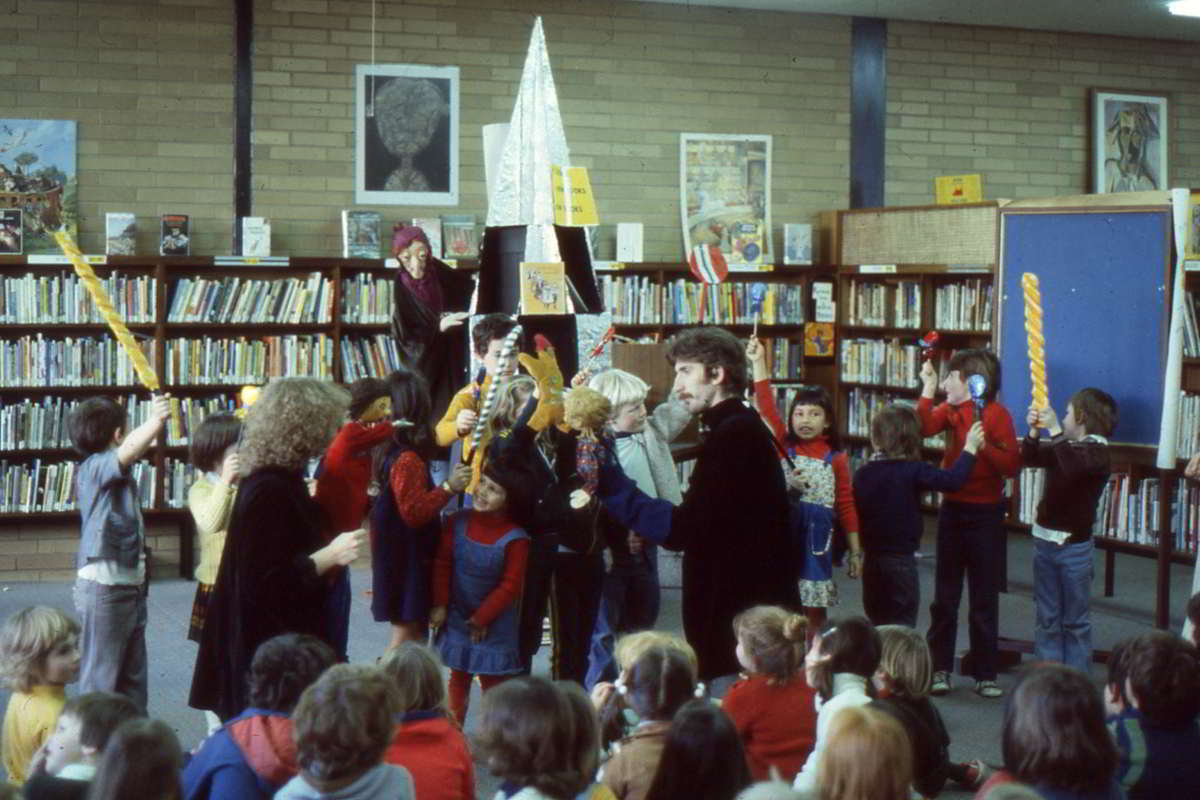performance in a library with witch in rear and puppeteers amongst a crowd of children