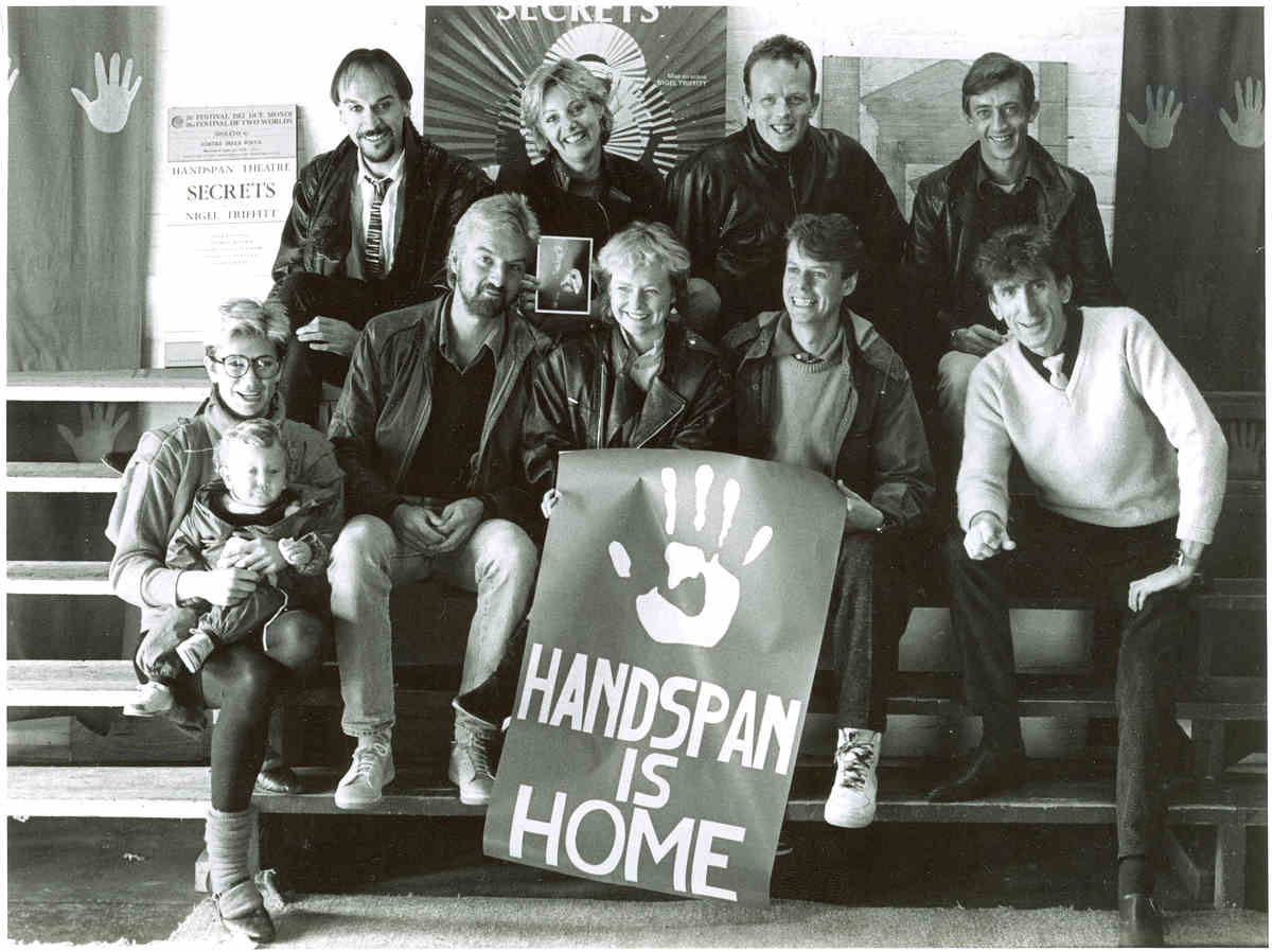 Handspan At Home people posed on bleachers with poster saying Handspan is Home