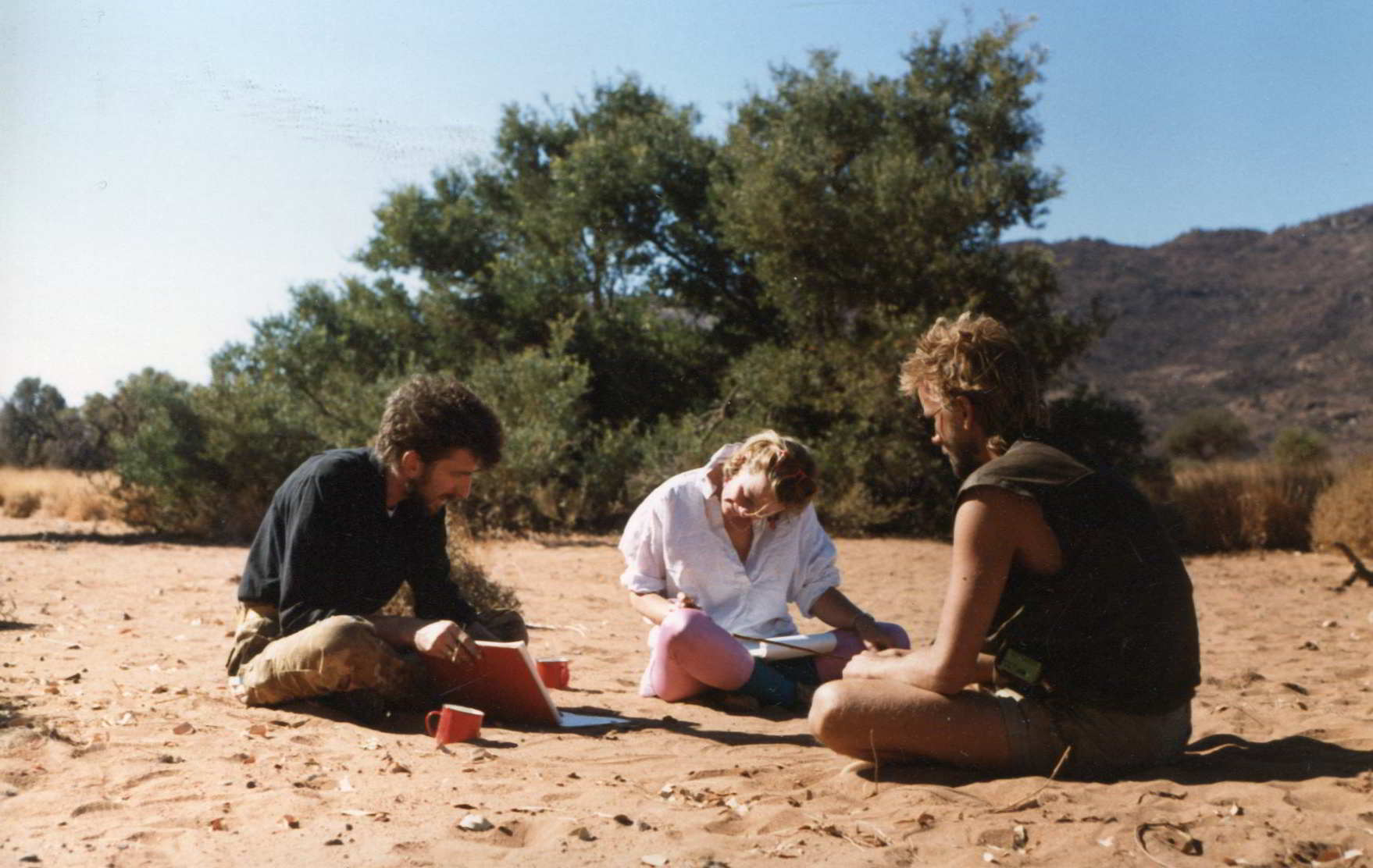 Handspan Theatre The Haunted 2 men and a woman at a working meeting sitting on desert ground
