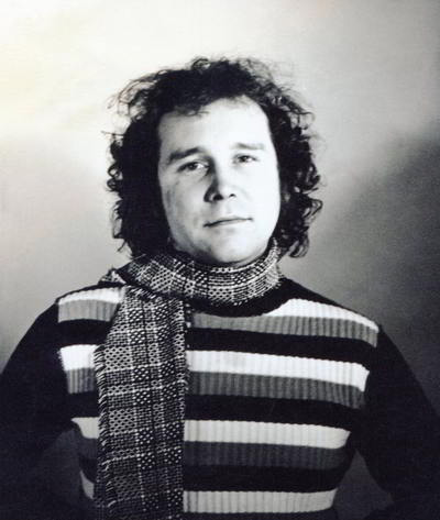 Handspan Theatre Roy McNeill portrait of round-faced man with curley hair wearing striped jumper and scarf