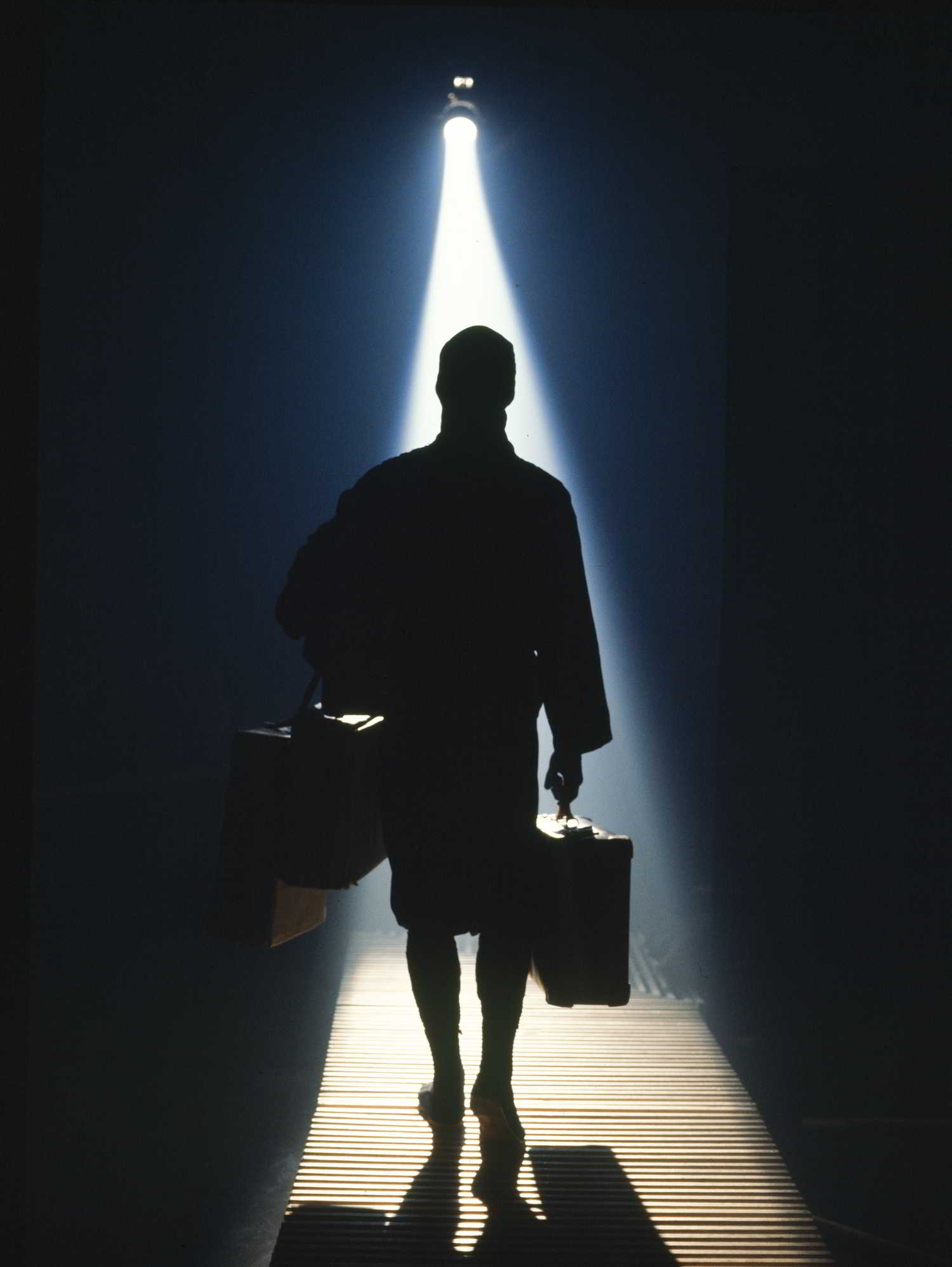 Secrets Handspan Theatre man carrying two suitcases, silhouetted against a shaft of light