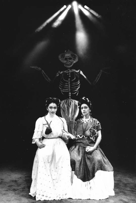 Handspan Theatre Viva La Vida - Frida Kahlo two women in long dresses seated in front of a looming skeleton in light beams