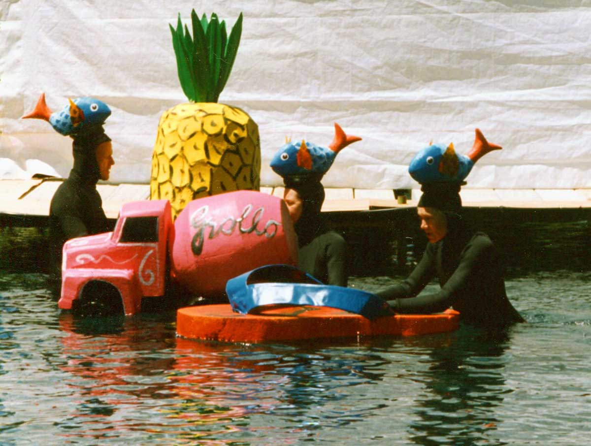 Handspan Theatre Waves of Change 3 puppeteers in wet suits with fish on their heads, operating a large floating pineapple, a thong and a cement mixer truck