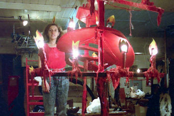 woman stands on workbench beside tall red candelabra