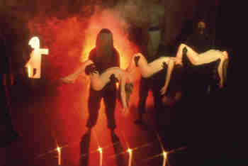 black-clad puppeteers carry sleeping girls in smoke and orange light