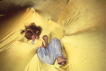 small girl asleep on large raised disc of yellow stretch fabric