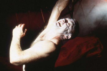 a man naked to the waist writhing in torment against a smoky red background