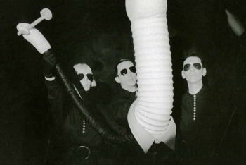 three puppeteers operating large phallic puppet wearing a suit