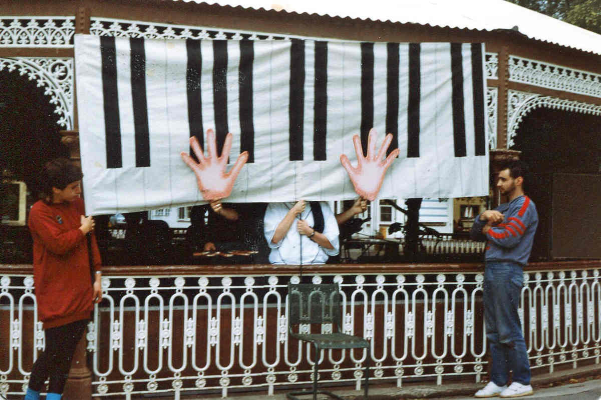 outside view of park rotunda with people holding up a large fabric banner representing piano keys played by 2 large foam hands on sticks