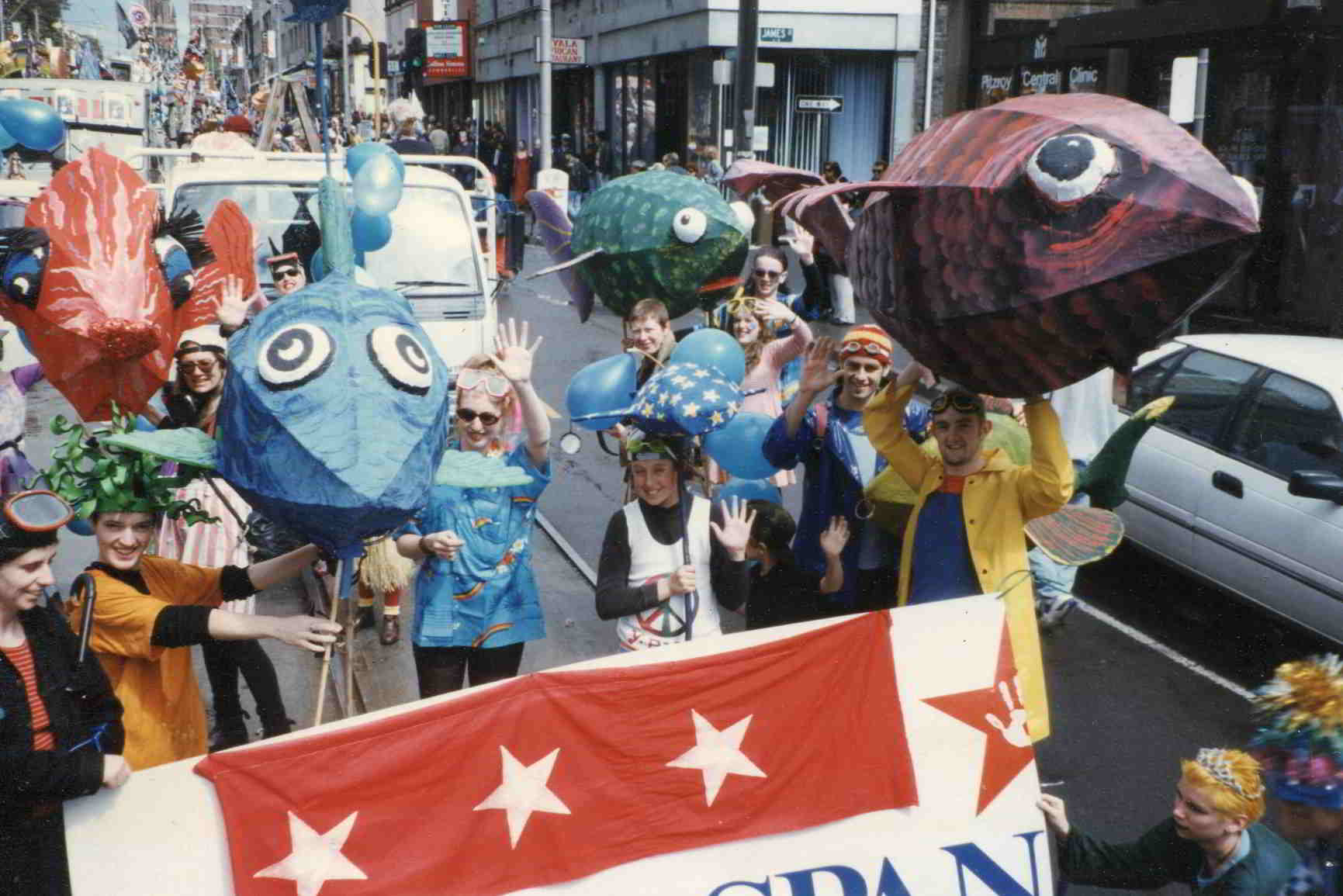 Swim Handspan Theatre large cane fish waving at overhead camera in crowded street parade