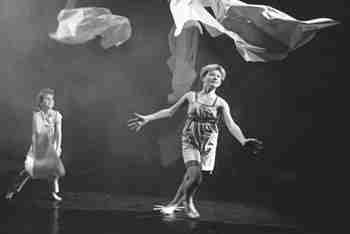 two girls chase lengths of white cloth swirling mid-air above them